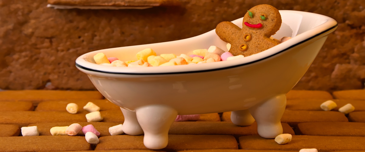 A small gingerbread man cookie sitting in a claw foot tub filled with tiny marshmallows
